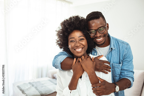 Happy mature black couple bonding to each other and smiling. Portrait of smiling black man embrace his wife from behind and looking at camera. Portrait of a happy young couple