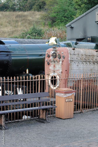 Vintage Steam Locomotive and Old Boiler beside  Railway Platform with Fence Bench and Waste Bin   photo