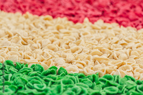 Fresh green, white and red orecchiette or orecchietta pasta drying under the sun on a wooden board, made with durum wheat and water, handmade pasta typical of Puglia, Apulia, Southern Italy, close up photo