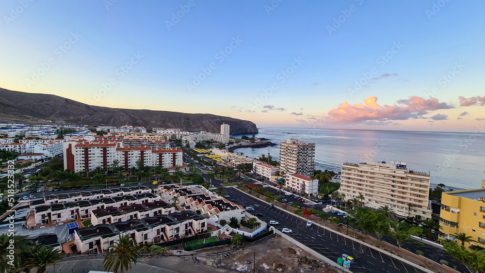 Romantic aerial sunset over the sea in summer seen from a tourist resort in Los Cristianos, Tenerife, Canary Islands, Spain, Europe. Vibrant colours of the clouds. Vacation vibes on the Atlantic Ocean