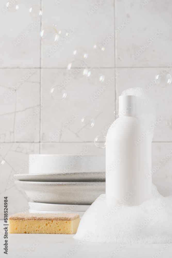 White bottle with dishwashing detergent and soap suds. Plates in the background. Washing dishes in the kitchen, cleaning concept White bottle with dishwashing detergent and soap suds. Plates in the background. Washing dishes in the kitchen, cleaning concept