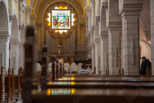 Beautiful white catholic church. The wooden benches of the church on which a man sits and prays. Cathedral for prayers with a beautiful interior. White columns of the church