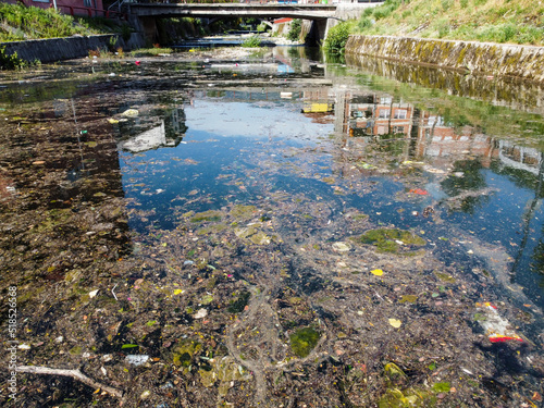 A polluted river in the city. Garbage in the river. Trash floating in water. Environmental problem. Plastic bags, bottles and garbage dumped in river. Environmental disaster.