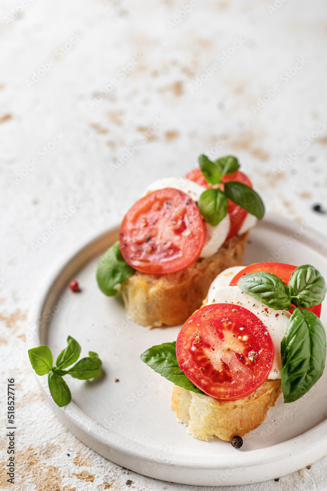 Italian bruschetta with tomatoes, mozzarella and basil on white plate with text space
