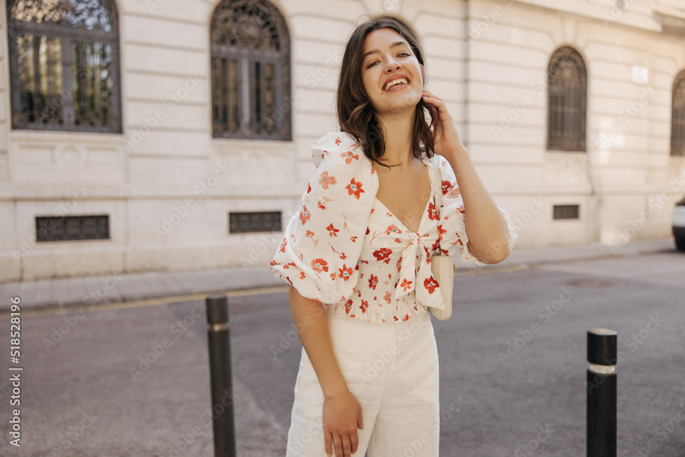 Joyful young caucasian woman looks at camera, enjoys walk in spring city. Brunette wears casual clothes from a blouse and pants. Relaxation concept Joyful young caucasian woman looks at camera, enjoys walk in spring city. Brunette wears casual clothes from a blouse and pants. Relaxation concept