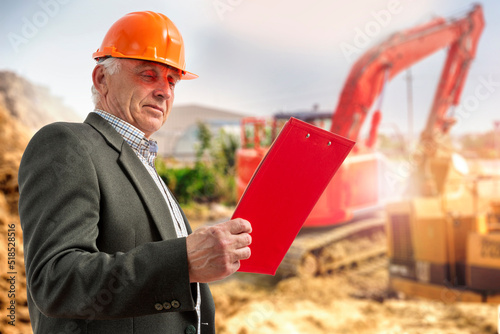 Construction supervisor, worker at a construction site. Manager wearing protective workwear, hard hat looking at clipboard, construction bulldozer, excavator. Construction workforce, working labor man