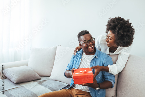 Romantic Couple Exchanging Christmas Gifts At Home. Husband And Wife Affectionately Exchanging Christmas Gifts. Wife making a surprise giving a present to her husband at home
