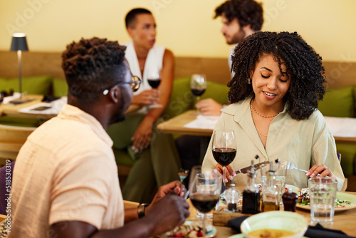 A happy multiracial couple sits in a restaurant  chatting and having dinner together.