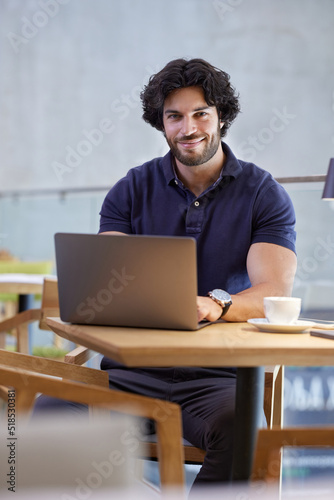 A young casual businessman is sitting in a coffee shop and typing on the laptop.