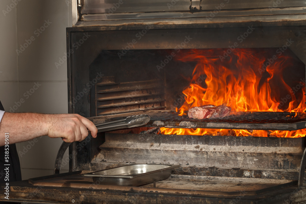 Chef makes beef steak on open fire in restaurant