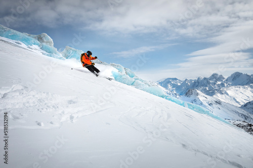 Off-piste skier on a glacier going down a beautiful alpine landscape. Blue cloudy sky in the background and high mountains. Free space for text