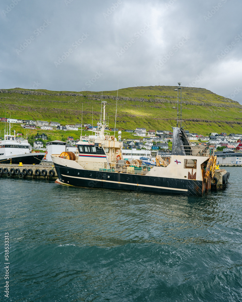 Klaksvik viewed from a ferry leaving the port. Calm water surface and steep green cliffs on a cloudy, rainy day in Faroe Islands. Klaksvik viewed from a ferry leaving the port. Calm water surface and steep green cliffs on a cloudy, rainy day in Faroe Islands.
