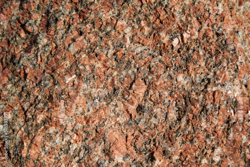 The texture of red stone with splashes of gray and white. Small crystals on the surface of the stone. Stone looks like a fragile building material.