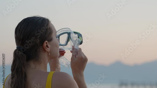 A girl tries on a mask for scuba diving against the background of the sunset sky and mountains. close-up photo