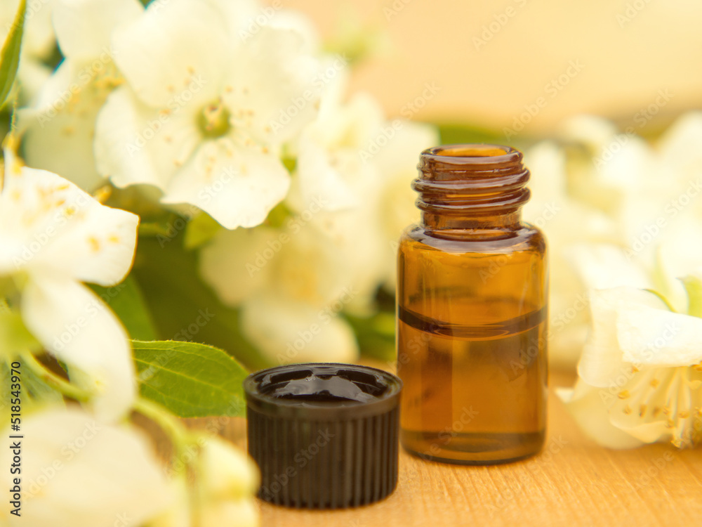 Jasmine essential oil in a glass bottle on a background of jasmine flowers on a wooden table Jasmine essential oil in a glass bottle on a background of jasmine flowers on a wooden table