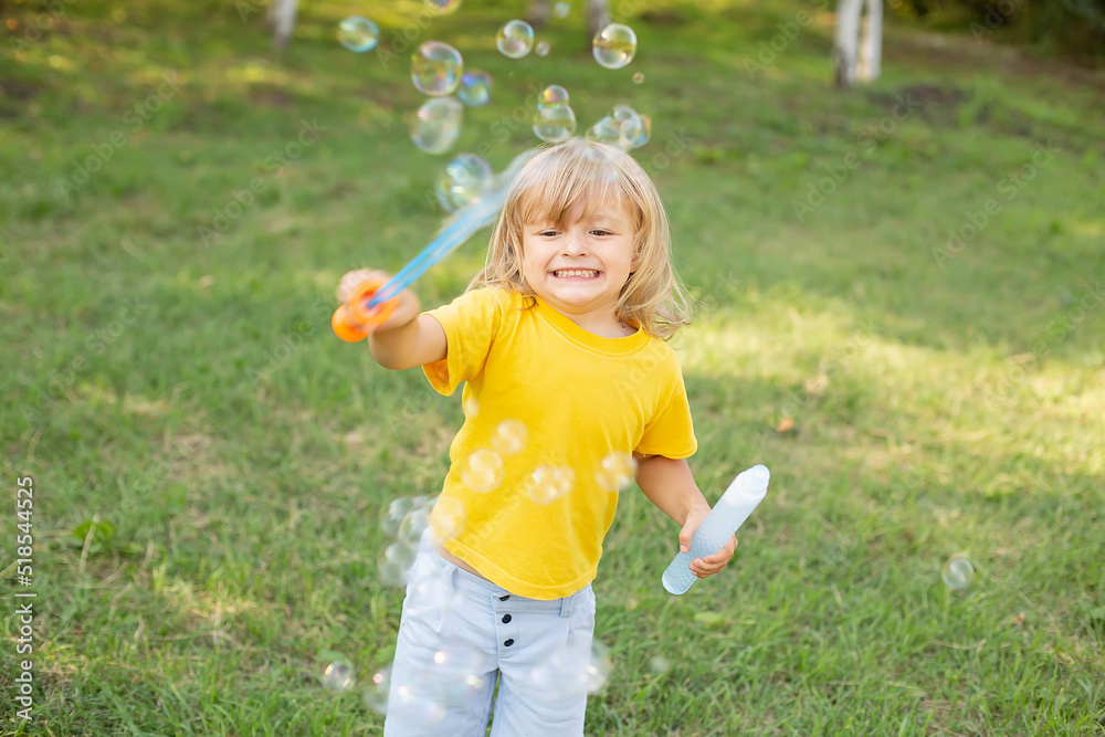 happy blond boy with long hair in a yellow T-shirt playing with soap bubbles happy blond boy with long hair in a yellow T-shirt playing with soap bubbles