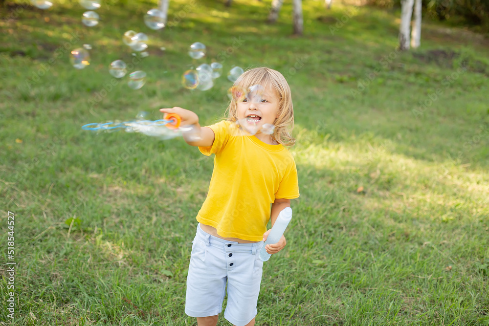 happy blond boy with long hair in a yellow T-shirt playing with soap bubbles happy blond boy with long hair in a yellow T-shirt playing with soap bubbles