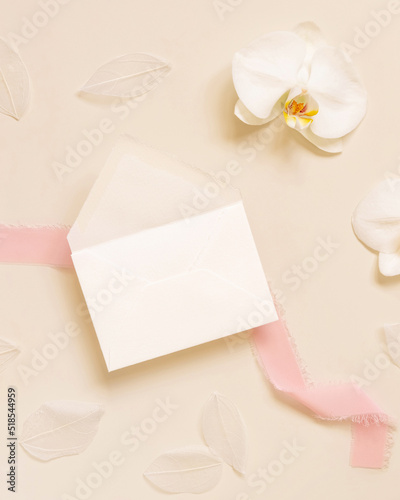 Wedding envelope near white orchid flower and silk ribbons on yellow, mockup
