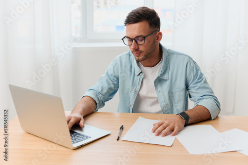 Serious happy handsome stylish young businessman in eyewear typing report for project looks aside reclines on table. Copy space for ad. Remote Job Technology And Career Profession Concept