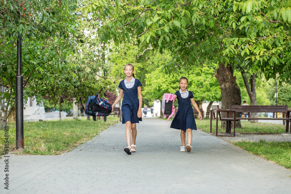 Two schoolgirls go from school and throw backpacks. Children are having fun. Concept back to school