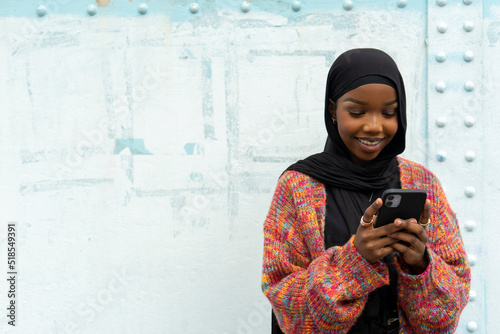 Cuadro en lienzo Smiling young woman wearing hijab looking at smart phone