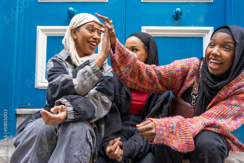 Fotografiet Three smiling women wearing hijabs sitting in front of blue door