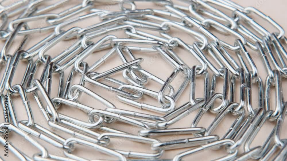 A metal chain with many shiny links rotates lying on a wooden surface folded in a circle in the center, close-up. A metal chain with many shiny links rotates lying on a wooden surface folded in a circle in the center, close-up.