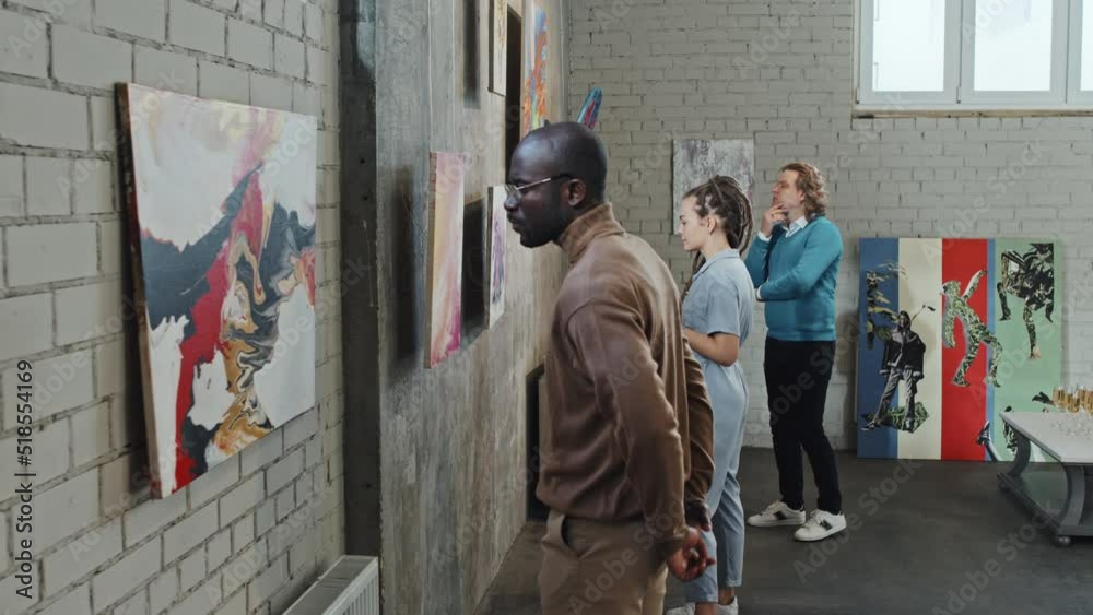 Three young people observing paintings in modern art gallery at daytime Three young people observing paintings in modern art gallery at daytime