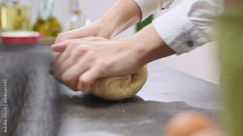 Female hands kneading dough on the table, slow motion.
