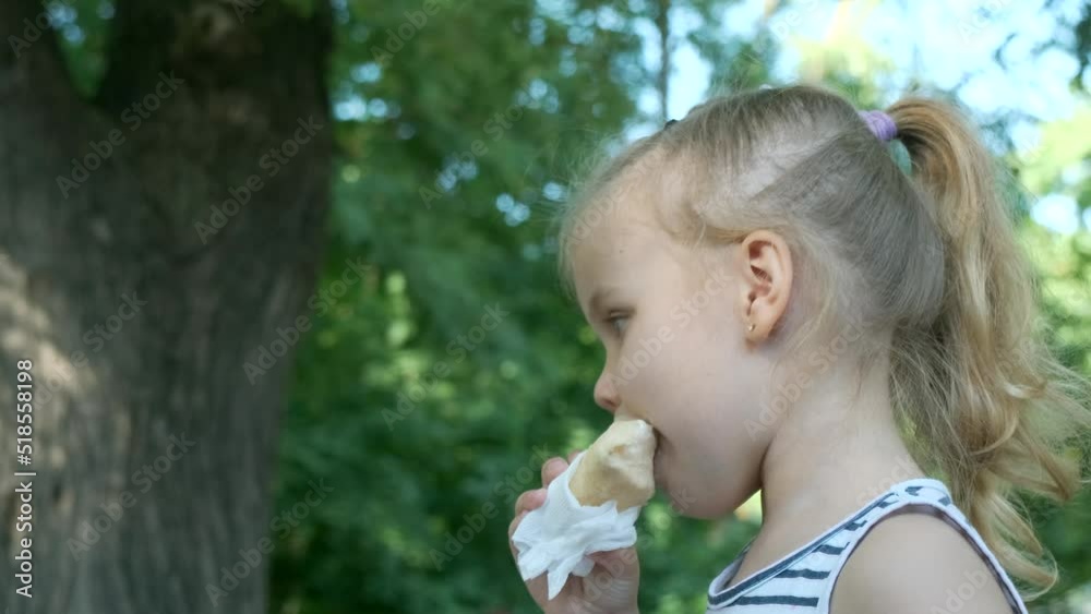 Little girl eats ice cream. Close-up portrait of blonde girl sitting on park bench and eating icecream. Slow motion, Camera slowly moving forwards. Little girl eats ice cream. Close-up portrait of blonde girl sitting on park bench and eating icecream. Slow motion, Camera slowly moving forwards.