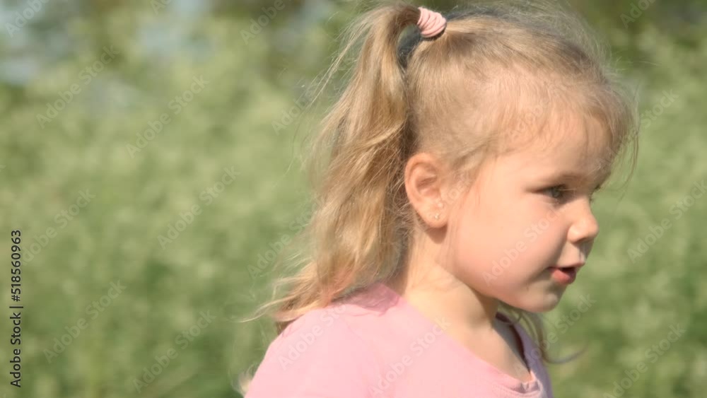 Close up portrait of little girl walks through tall grass and plays with soap bubbles in park. Cute little girl spinning, smiles and blows soap bubbles in meadow on sun day. Slow motion Close up portrait of little girl walks through tall grass and plays with soap bubbles in park. Cute little girl spinning, smiles and blows soap bubbles in meadow on sun day. Slow motion