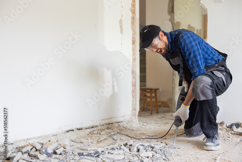 Removal of old floor during renovation of apartment. The idea of working by hand. Close-up of chisel from demolition hammer, fragments of ceramic tiles, dust. Male worker puts all strength into work.