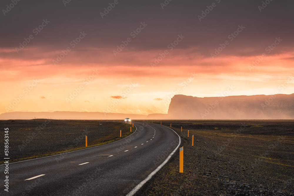Scenic curved asphalt road with car driving and sunset sky on mountain at Iceland