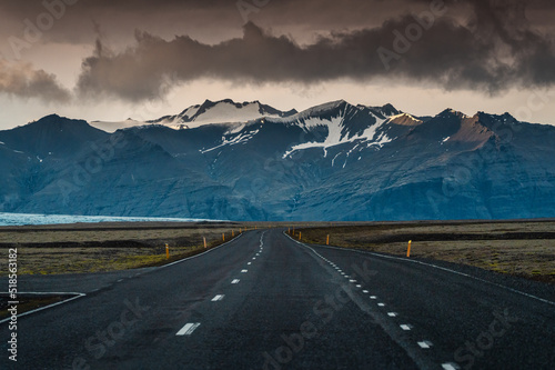 Straight asphalt road with storm over mountain on gloomy day in Iceland
