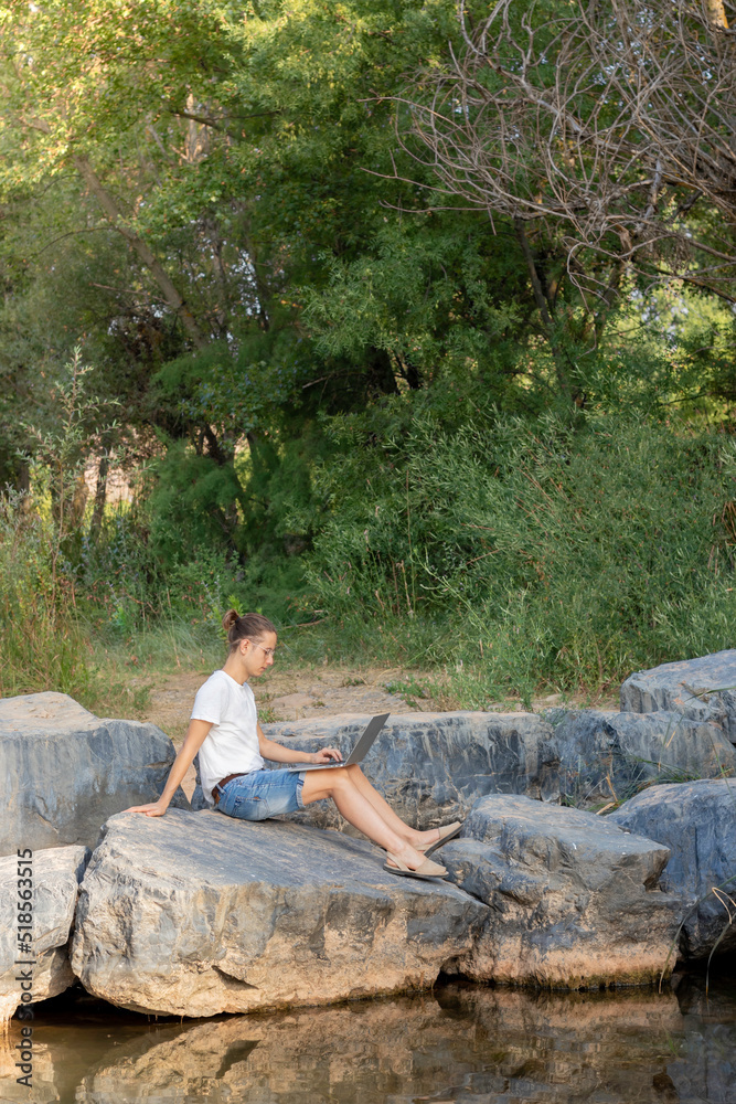 Vertical vision of a remote worker sitting on the bank of a river and working with his laptop in nature Vertical vision of a remote worker sitting on the bank of a river and working with his laptop in nature