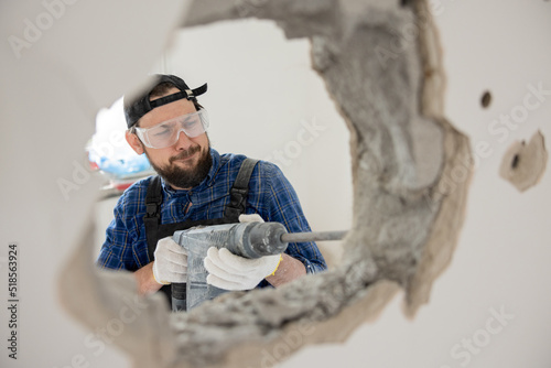Focused on his work, a construction worker drills with a hammer to demolish a wall in a house under renovation, demolishing the interior of an apartment a hole through and through.