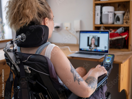 Woman in electric wheelchair having video call on laptop photo