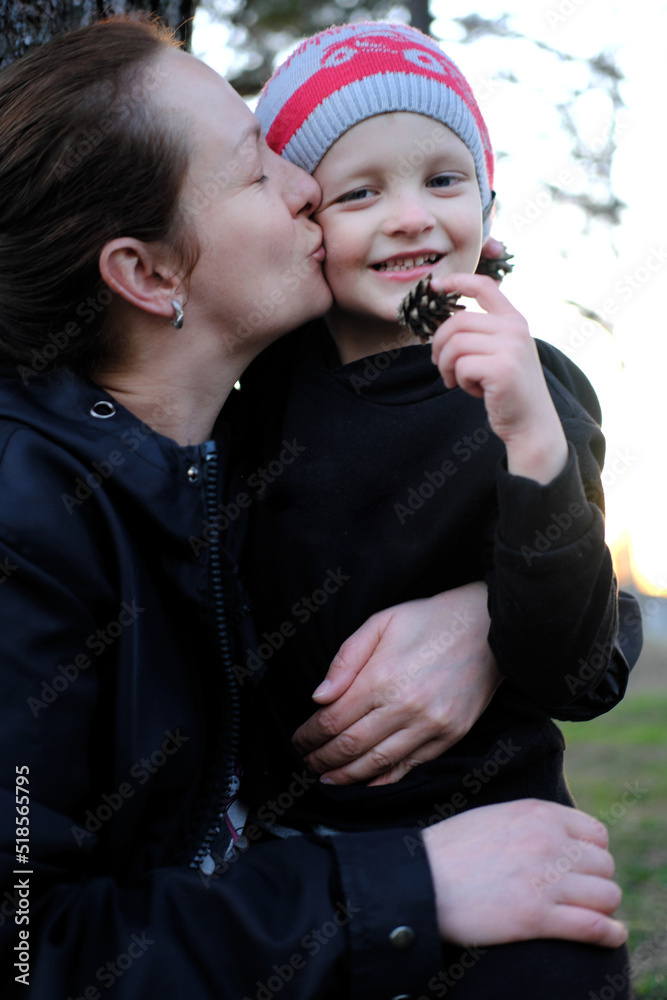 Mother and little son spend time together in the park in the evening. Mother kissing her son. Mother and little son spend time together in the park in the evening. Mother kissing her son.