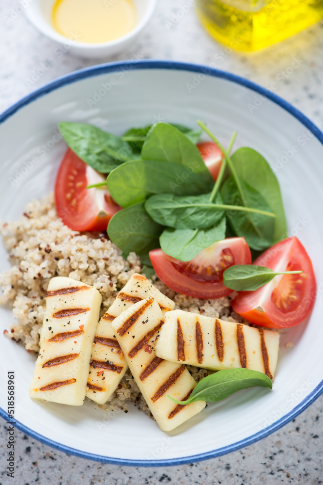 Quinoa with grilled halloumi, fresh spinach and red tomatoes, vertical shot, closeup, selective focus