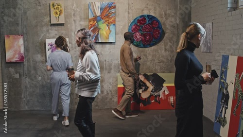 Diverse people walking and looking at paintings in contemporary art gallery at daytime photo