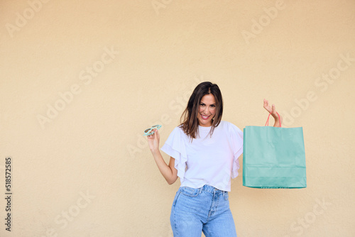 happy young woman enjoying a day of shopping with a bag in one hand and sunglasses in the other.