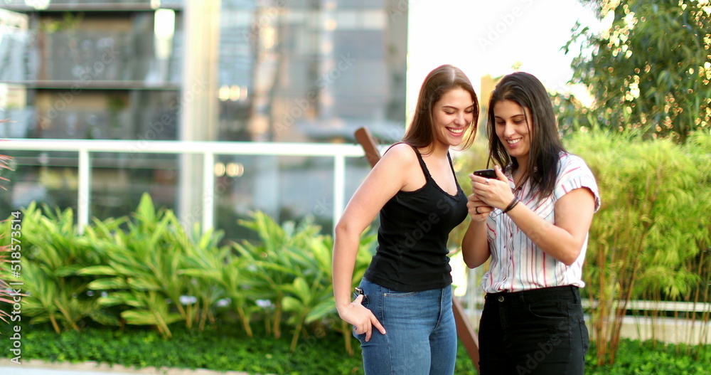 Naklejka premium Two young women looking at smartphone device laughing and smiling