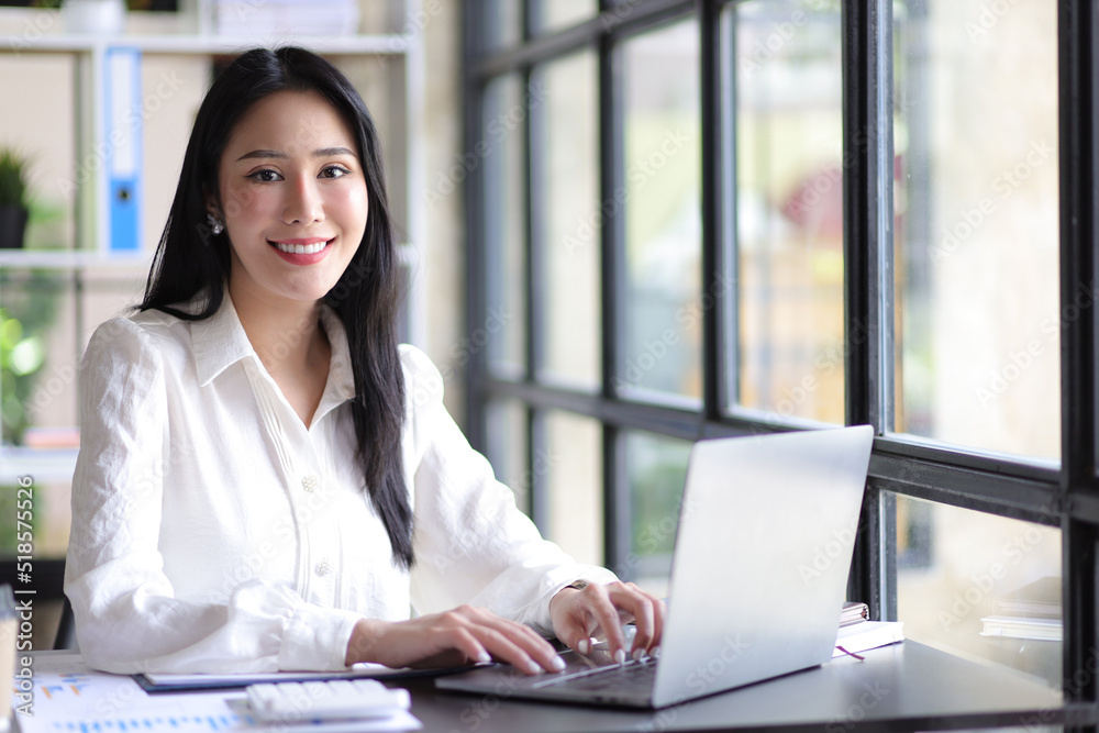 Casually dressed Asian woman working on laptop and documents in home office. Work from home concept. Casually dressed Asian woman working on laptop and documents in home office. Work from home concept.