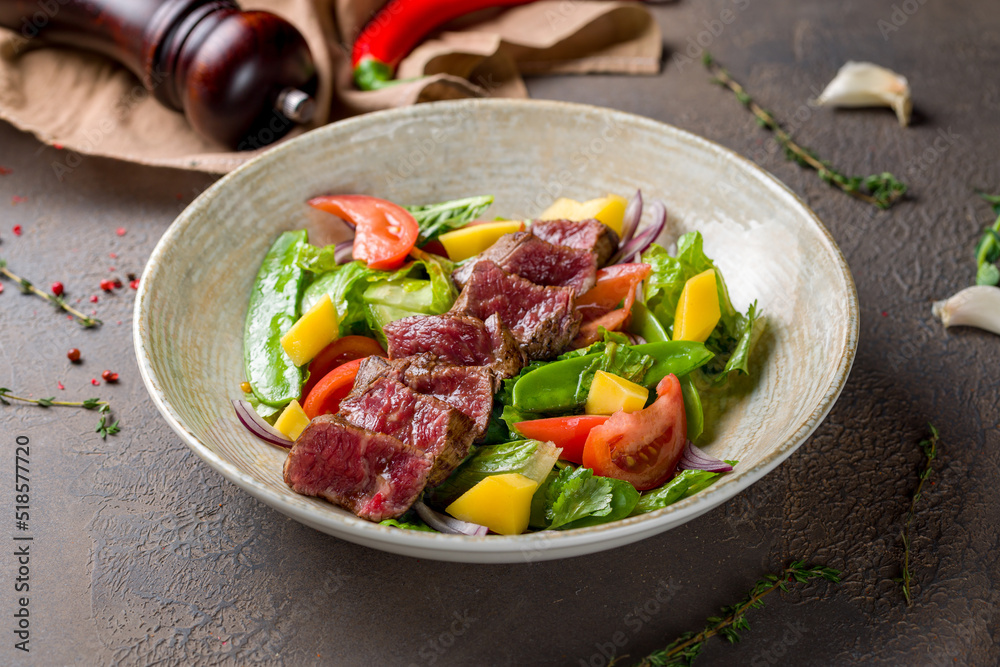 Steak salad with beef and vegetables on plate on brown table Steak salad with beef and vegetables on plate on brown table