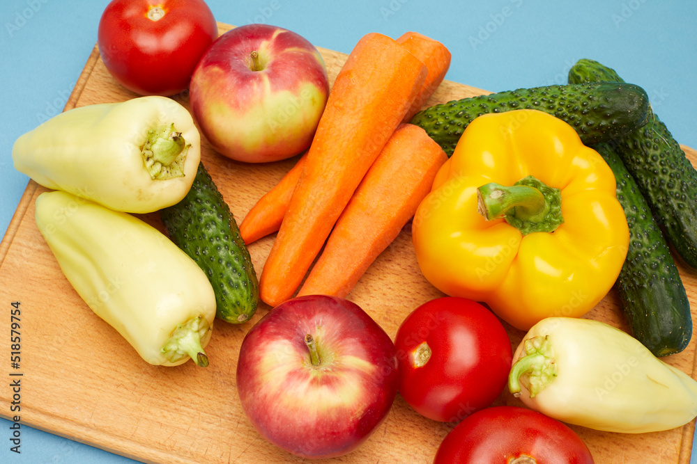 Close up view of vegetables and fruit on wooden cutting board over on blue background. Close up view of vegetables and fruit on wooden cutting board over on blue background.