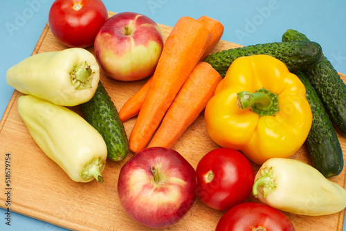 Close up view of vegetables and fruit  on wooden cutting board over on blue background.