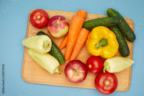 Close up view of vegetables and fruit  on wooden cutting board over on blue background.