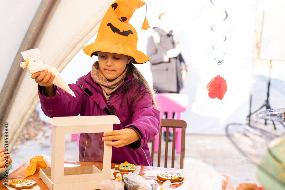 Little kids at a Halloween party. Little girl decorates cookies for Halloween Little kids at a Halloween party. Little girl decorates cookies for Halloween