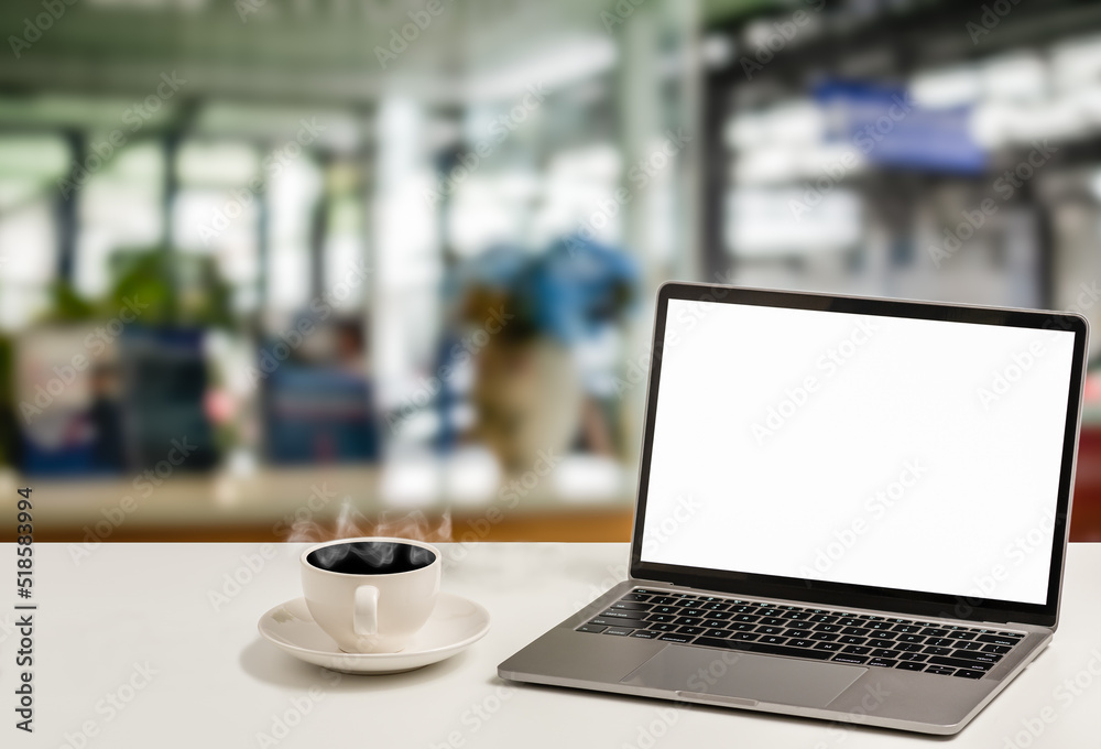 Fototapeta premium A blank white screen laptop and coffee cup are placed on a white desk in an office. The Concept for business, technology, internet, design, and art. Closeup, selective focus, blurred background