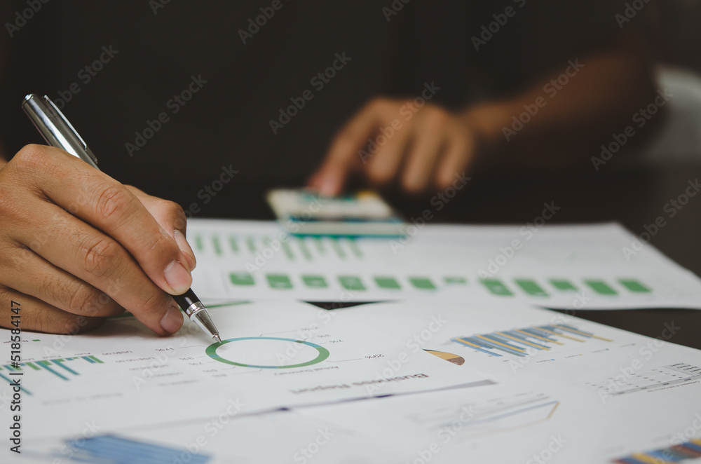 Businessman hand holding pen pointing paperwork chart report analysis statistic and document financial graph investment marketing on desk in company. Businessman hand holding pen pointing paperwork chart report analysis statistic and document financial graph investment marketing on desk in company.
